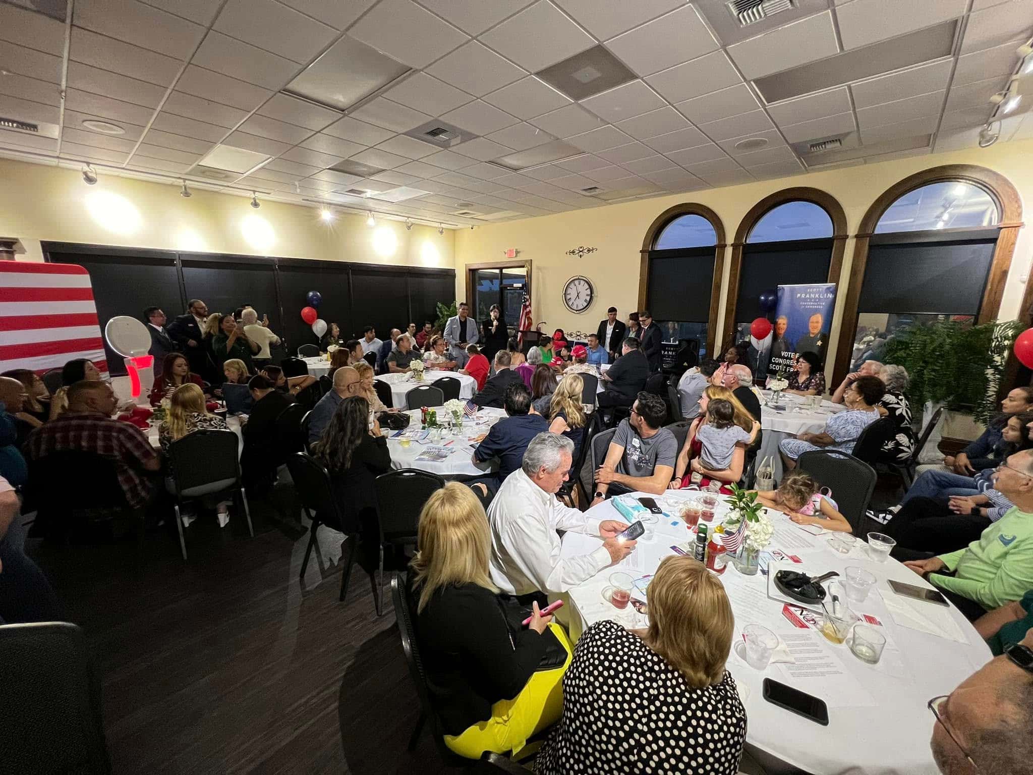A packed Polk County Republican Executive Committee meeting, with attendees seated at tables and an American flag along the wall